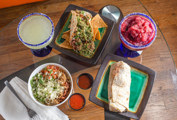 Tasty margaritas and Mexican food on glass table shot from overhead