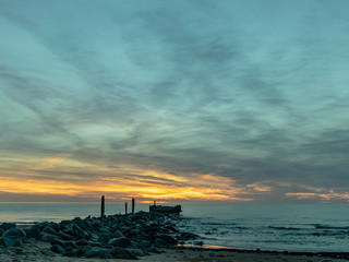 landscape with defocused beautiful dramatic sky over the sea,  stone pier in the background, reflection at sunset time, long exposure 
