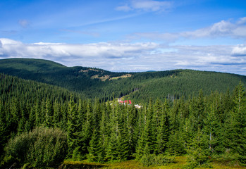 Fototapeta na wymiar Mountain forest landscape with a red house far.