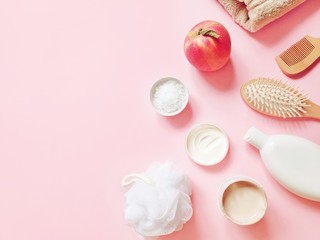 Natural fruits cosmetics on a light pink background. White shampoo bottle, wooden hair brush, sea salt scrub, kaolin clay face mask, nourishing cream with essential oils