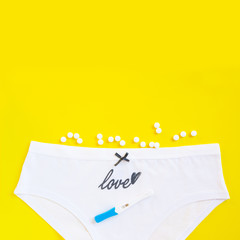 Female white panties with bow, birth control pills or vitamin and pregnancy test on yellow background. Health care, contraception and planned pregnancy.