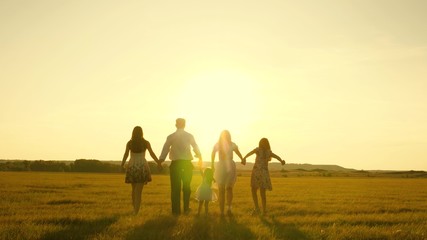 mother, father and little daughter with sisters walking in the field in sun. Happy young family. Children, dad and mom play in the meadow in the sunshine. The concept of a happy family.