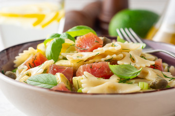 Farfalle pasta salad with smoked tuna, avocado, capers and greens in bowl on concrete background. Selective focus.