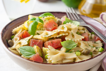 Farfalle pasta salad with smoked tuna, avocado, capers and greens in bowl on concrete background. Selective focus.