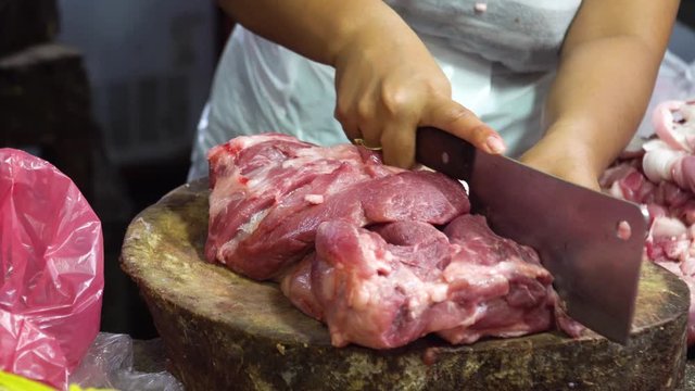 Butcher chopping and cutting meat for sale at a street market, Philippines. Butcher chopping raw meat with a knife on a wooden board in a street market. Butcher hands close up: cutting meet