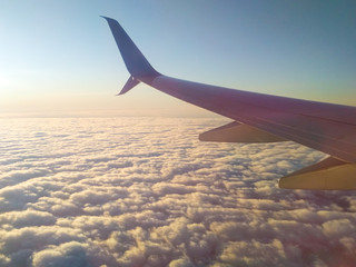 Obraz premium wing of a flying airplane over dense white clouds in the light of the rising sun