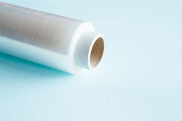 Roll of transparent polyethylene food film for packing products on pastel blue table. Empty place...