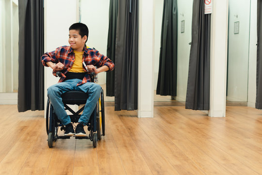 Disabled child on wheelchair having fun shopping for clothes, He is in front of fitting room,Special children's lifestyle,Life in the education age of special need kids,Happy disability kid concept.