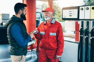 Young handsome adult man together with senior worker standing on gas station and fueling car.