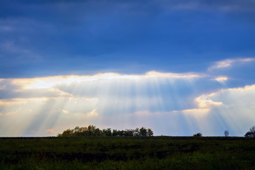Naklejka na ściany i meble Landscape with a beautiful sky and rays of sunshine penetrating through dark cloud_