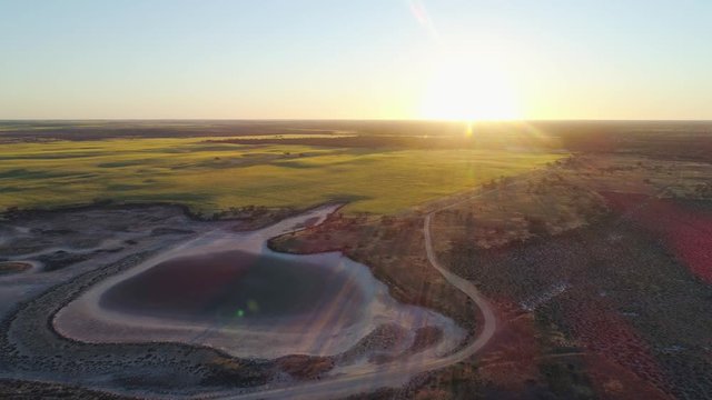 Forward flight over desrt towards agricultural fields with sun flare at sunset in Australia