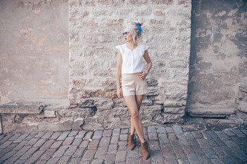 Fototapeta na wymiar Young skinny stylish lady in shorts posing in sunglasses in front of the wall and in the cafe