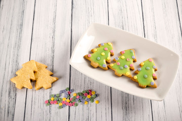 Top view of delicious Christmas trees made of gingerbread cookies decorated with green frosting and colored sugar confetti on a background that simulates a rustic wooden table. Christmas desserts