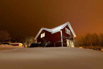 Typical Swedish red wooden house, winter garden with fruit trees, huge snowdrifts, the sky is...