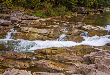 Beautiful mountain river with a fast flow. Large stones with rocks in the middle of a green forest.