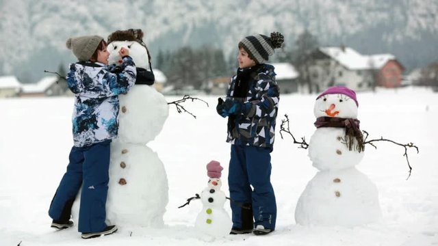 Family with children, building snowman in the park in little village in Austria, beuatiful landscape scenery