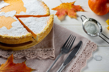 Pumpkin pie with leaves. Sieve, cutlery and napkin. Autumn white rustic wood background