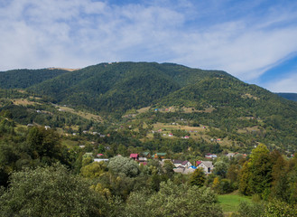 Fototapeta premium Mountain forest green landscape with houses and a far village.