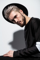 Handsome guy in black clothes with the hat on his head and stylish hairdo. Male model with ashen hair.
