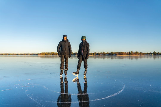 Two teenage boys are posing for memory photo before ice skating - on the crystal clear frozen lake. The big frozen lake in Northern Sweden - ice like natural mirror.