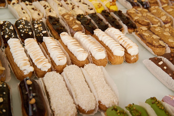 Lots of cream cakes close-up. Eclairs of different colors