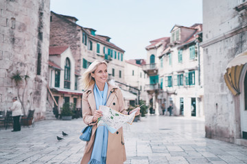 Fototapeta na wymiar Travel and active lifestyle concept. Young traveller woman walking on old town holding tourist map.
