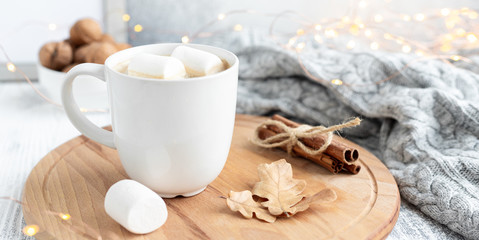 Obraz na płótnie Canvas A mug of coffee with marshmallow, sweater, cinnamon, decorated with led lights. Cozy christmas composition. Horizontal banner. Hygge concept. Soft focus