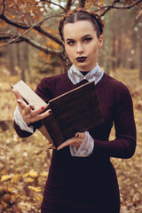 Halloween Beautiful young Witch girl in witches dress on autumnmagic forest background. witch with magic Book of spells.