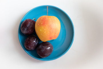 plums and yellow apple on a blue plate
