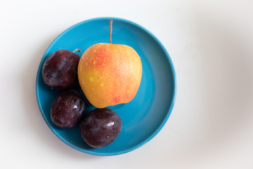 plums and yellow apple on a blue plate