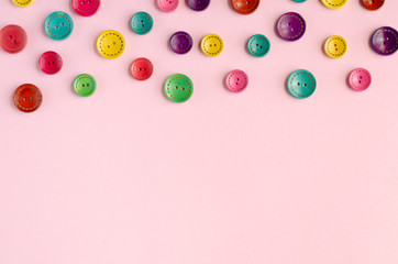 Colored sewing buttons composition on pink background.