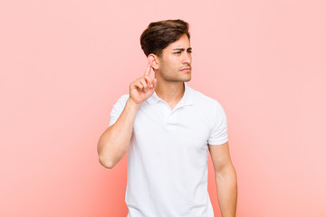 young handsome man looking serious and curious, listening, trying to hear a secret conversation or...