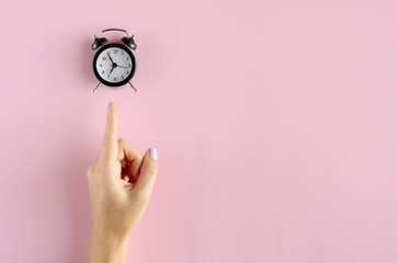 Hand with analog alarm clock composition on pink background.