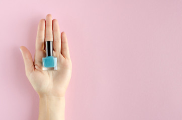 Hand with colored nail polish composition on pink backgorund.