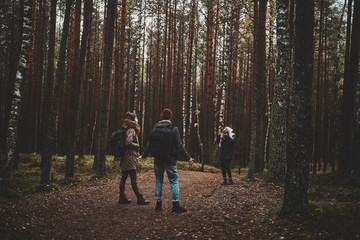 Young blond woman is making a photo of her friends in the deep autumn forest.