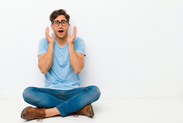 young handsome man feeling shocked and excited, laughing, amazed and happy because of an unexpected...