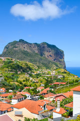 Fototapeta na wymiar Picturesque village Porto da Cruz in Madeira island, Portugal. Houses on the green hills, rock formation, cliff by the Atlantic ocean in the background. Hilly terrain. Portuguese landscapes