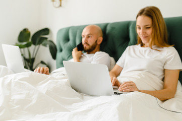 young couple uses laptop in bed. freelancer morning.
