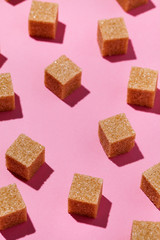Geometry pattern made of brown sugar cubes on trendy pastel pink color background with hard shadows.Abstract,minimal style.Vertical orientation