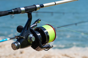 Fishing carp reel close-up on the background of water and fishing rods in a bright Sunny day. Background
