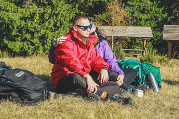 Fototapeta premium Girl and man hikers in mountains. They drink tea and coffee on top. Embrace. Campaign. Ukrainian Carpathian Mountains. Traveling in Ukraine.