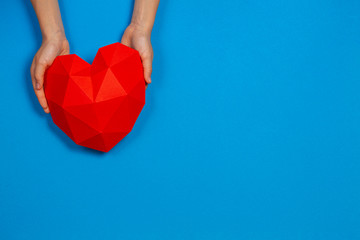 Hands holding red polygonal paper heart shape on light blue background