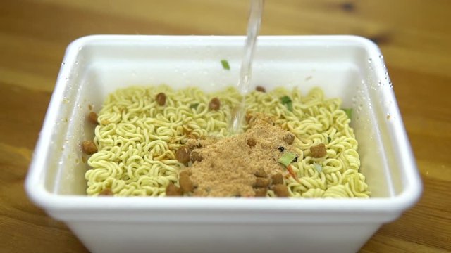 Instant noodles with spices are poured with hot water. Ramen in a plastic plate. Drops splash in different directions. Slow motion
