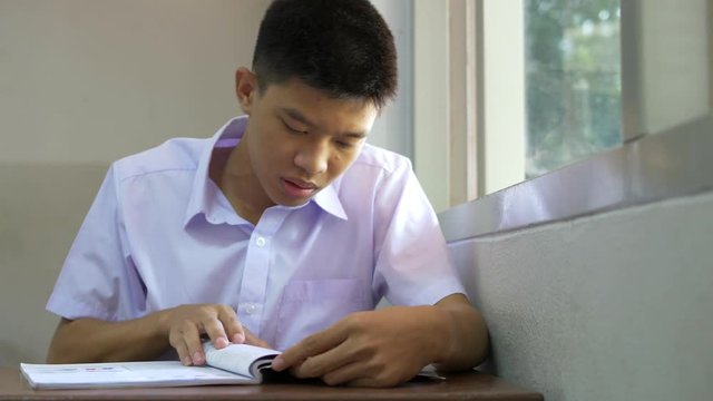 Male Asian high school student is reading a book in the classroom.