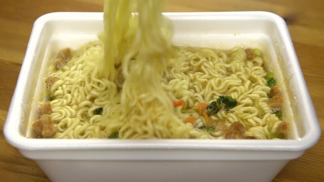 Instant noodles are mixed with Chinese chopsticks. Brewed yellow ramen in a special plastic plate