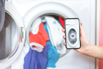 Woman is using a mobile phone for remote control of washing machine concept. Smart home.