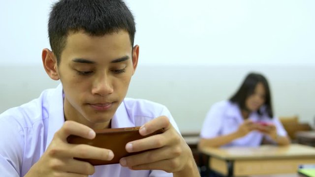 Asian high school students in a white uniform, who are a lot of addicted to games. They are playing exciting games on  their mobile phones and sitting in the classroom.