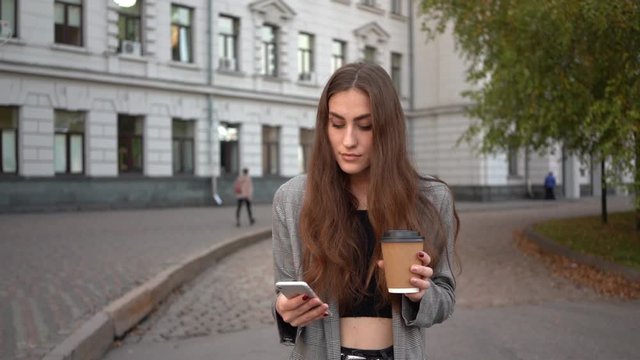 Woman girl student outdoors drinking coffee using mobile phone.