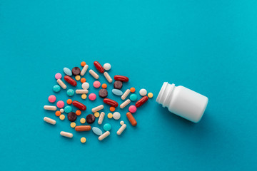 A handful of colored pills spilled out of the can on a blue background. Medical concept