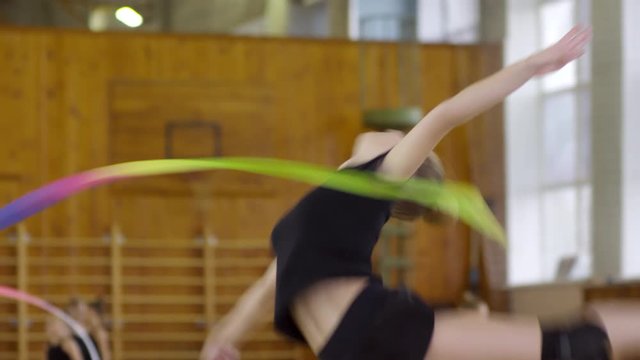 Teenage girl in sports clothes dancing with colorful ribbon when training in rhythmic gymnastics class